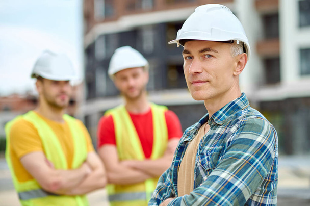 Three men in protective helmets standing on the building site - Foto, afbeelding