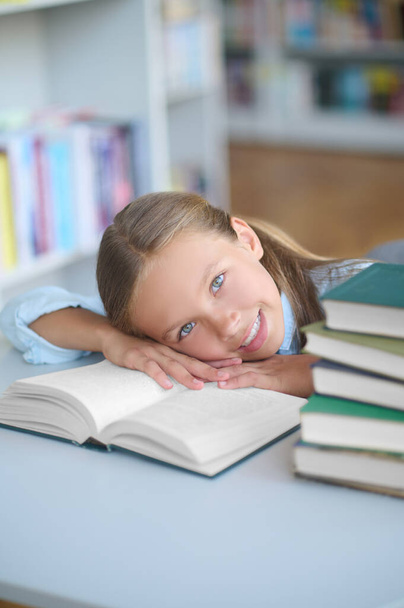 Joyous pretty schoolgirl lying on a library book - Zdjęcie, obraz