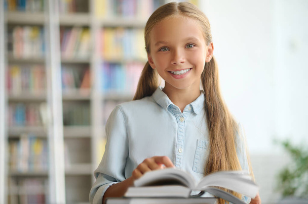 Happy cute schoolchild standing at a desk with books - Fotó, kép