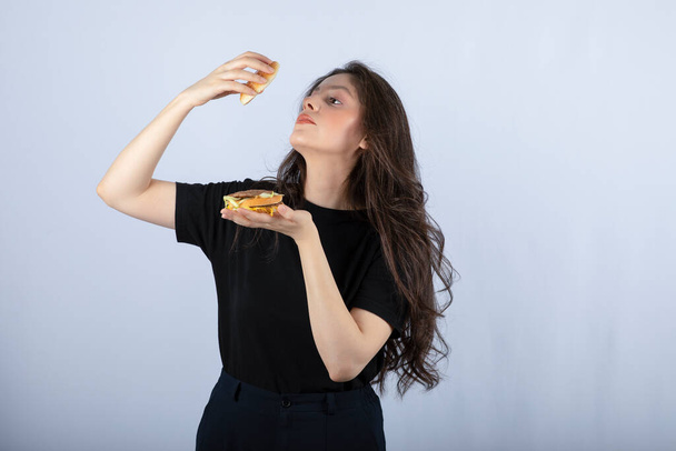 Retrato de mulher positiva posando com delicioso hambúrguer no fundo branco. Foto de alta qualidade - Foto, Imagem