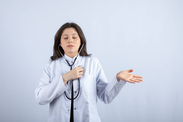 Young female doctor using stethoscope to check pulse on white background. High quality photo - Photo, Image