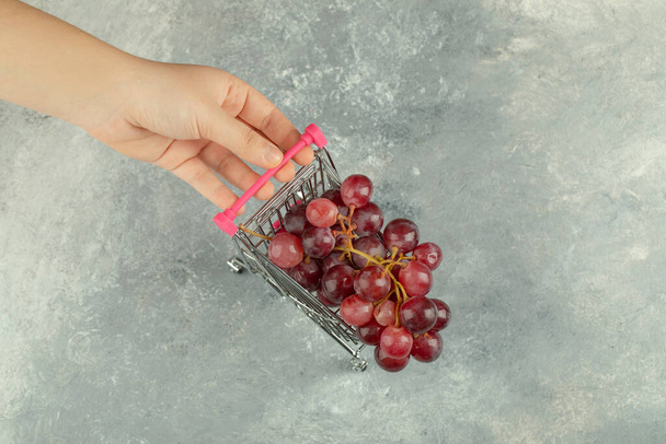 Vrouwelijke hand met metalen trolley van rode druiven op marmeren oppervlak. Hoge kwaliteit foto - Foto, afbeelding