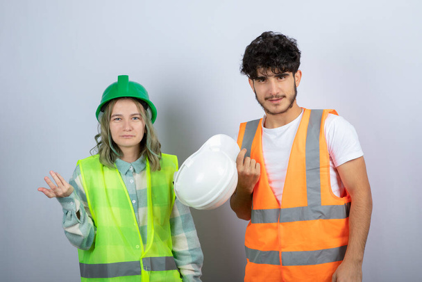 Deux jeunes ingénieurs féminins et masculins debout et posant sur un mur blanc. Photo de haute qualité - Photo, image