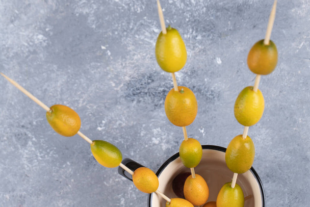Una taza llena de palillos con kumquats maduros sobre un fondo de mármol. Foto de alta calidad - Foto, Imagen