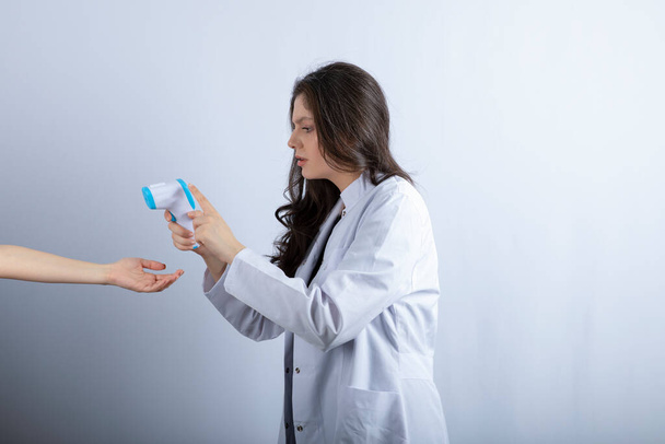 Egy női orvos hőmérővel, aki valakinek a hőmérsékletét méri. Kiváló minőségű fénykép - Fotó, kép