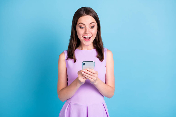 Phot of amazed positive young lady wear purple outfit hold smartphone novelty isolated on blue color background - Foto, afbeelding