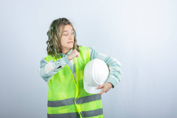 Foto eines jungen Bauarbeiters in grüner Weste, der einen Hut auf weißem Hintergrund hält. Hochwertiges Foto - Foto, Bild
