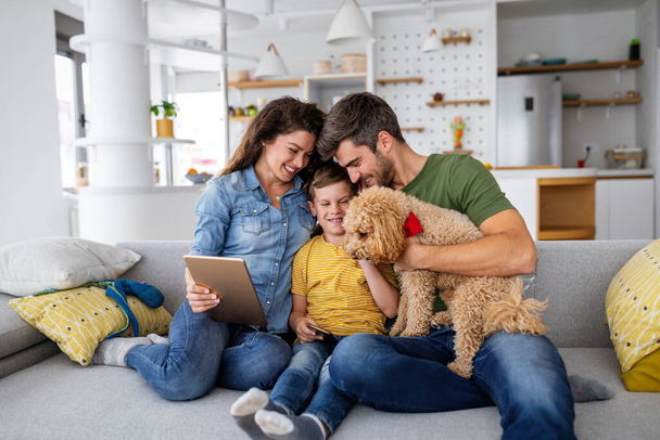 Happy young family with modern devices and dog having fun, playing at home - Foto, Bild