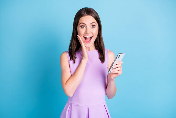 Photo of shocked happy young lady hold phone hand cheekbone amazed isolated on blue color background - Φωτογραφία, εικόνα