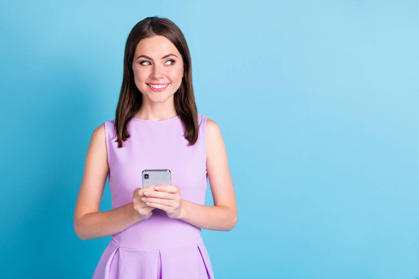 Photo of creative happy young lady look empty space hold phone imagine post isolated on blue color background - Photo, Image