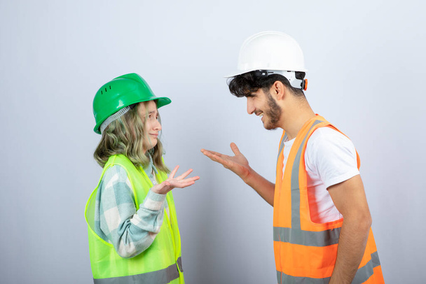 Jóvenes ingenieros guapos en cascos hablando entre sí sobre la pared blanca. Foto de alta calidad - Foto, Imagen