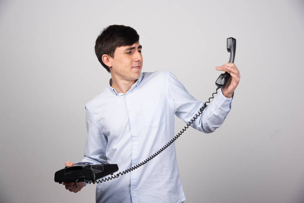 Черный стационарный телефон в руке мужчины на сером фоне. Высокое качество фото - Фото, изображение