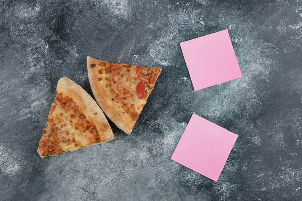 Dos rebanadas de deliciosa pizza fresca y papeles rosados sobre fondo de piedra. Foto de alta calidad - Foto, imagen