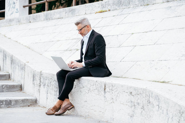 Uomo d'affari computer portatile di lavoro mentre seduto sulle scale nel centro della città - Foto, immagini