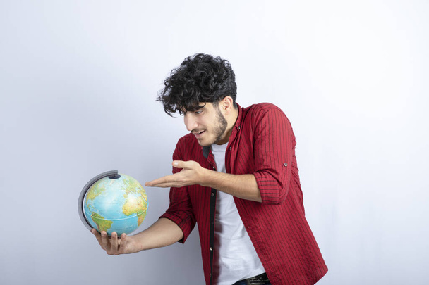 Porträt eines jungen Mannes, der eine Weltkugel gegen eine weiße Wand hält. Hochwertiges Foto - Foto, Bild
