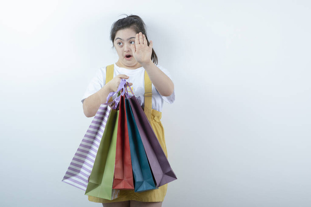 Entzückendes junges Mädchen mit Down-Syndrom, das Einkaufstüten auf weißem Hintergrund hält. Hochwertiges Foto - Foto, Bild