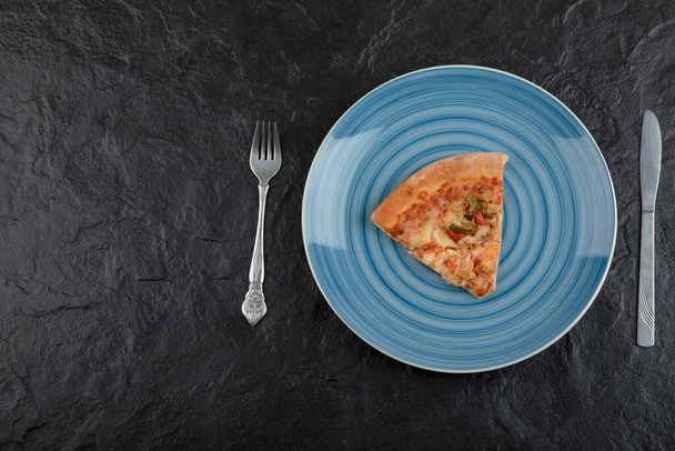 Plato azul de deliciosa rebanada de pizza sobre fondo negro. Foto de alta calidad - Foto, Imagen