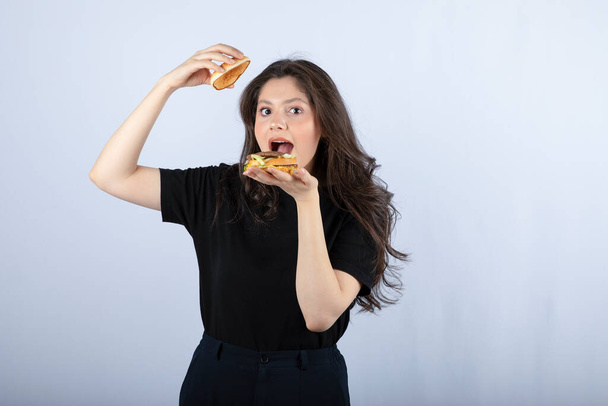 Portrét pozitivní ženy pózující s lahodným burger na bílém pozadí. Kvalitní fotografie - Fotografie, Obrázek