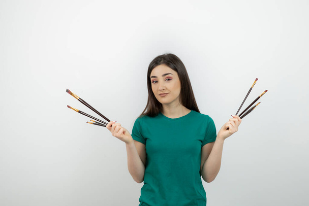 Photo of beautiful artist-girl standing and holding paintbrushes . High quality photo - Φωτογραφία, εικόνα