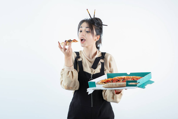 Een jonge vrouw die een doos met heerlijke pizza vasthoudt en een stuk pizza eet. Hoge kwaliteit foto - Foto, afbeelding