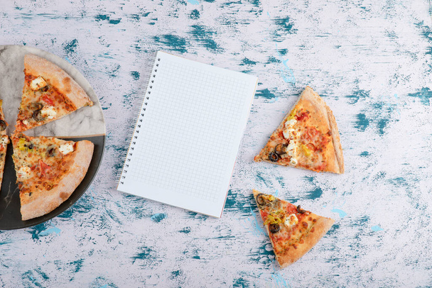 Slices of hot pizza with notebook on a marble background . High quality photo - Photo, Image