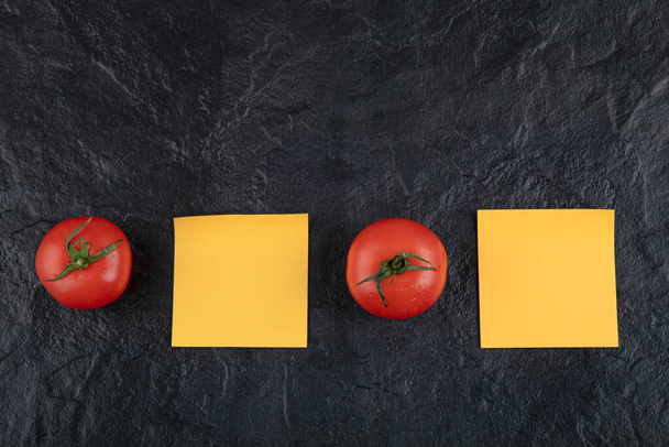 Two fresh red tomatoes with orange stickers on a black background . High quality photo - Photo, Image