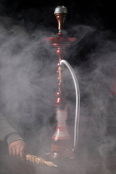 close-up. Hookah with a glass flask and a metal bowl hookah, there is a smoke of smoke. Black background. Front view - Photo, Image