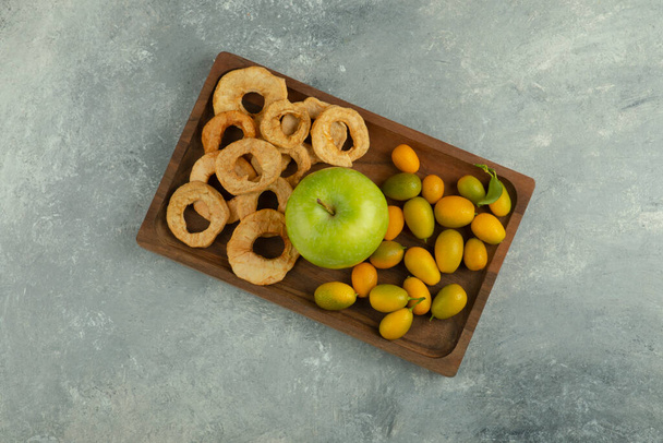 Дерев'яна тарілка із сушених яблучних кілець, зелене яблуко та кванти на мармуровій поверхні. Високоякісна фотографія
 - Фото, зображення