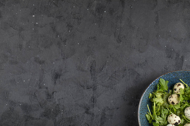 Piatto blu di uova di quaglia crude fresche e foglie di prezzemolo su sfondo nero. Foto di alta qualità - Foto, immagini