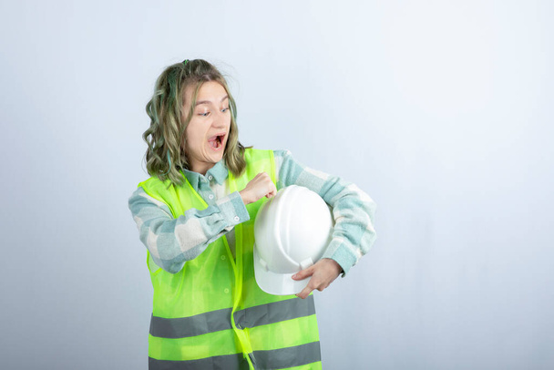 Foto de un joven trabajador de la construcción en chaleco verde que sostiene el sombrero sobre fondo blanco. Foto de alta calidad - Foto, imagen