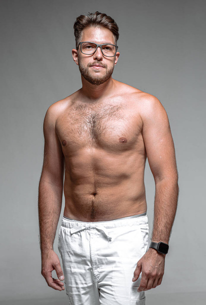 Young 30s male in glasses with naked torso. Overeating, fatness, overweight, physical inactivity and slimming concept - Фото, изображение