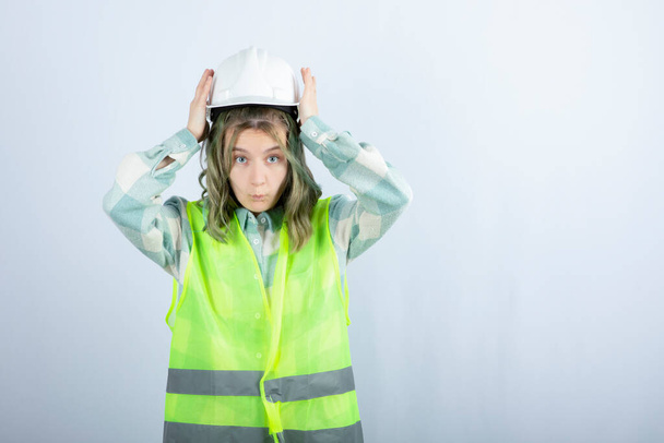 白い背景に硬い帽子をかぶって緑のベストで若い建設労働者の写真。高品質の写真 - 写真・画像