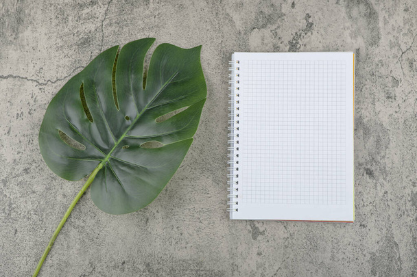 Τεχνητό πράσινο φύλλο και άδειο σημειωματάριο σε πέτρινο φόντο. Υψηλής ποιότητας φωτογραφία - Φωτογραφία, εικόνα