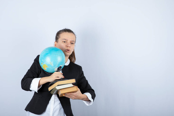 Photo of young teacher holding books and globe on white background. High quality photo - Photo, Image