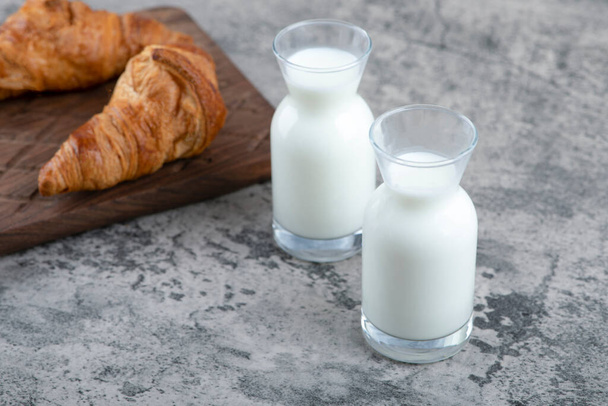 A wooden cutting board of fresh croissants and white glass pitchers of milk . High quality photo - Photo, Image