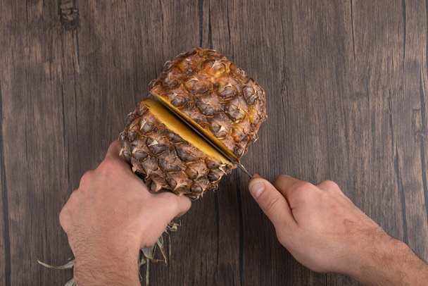 木製の背景に熟したパイナップルを切断男性の手。高品質の写真 - 写真・画像