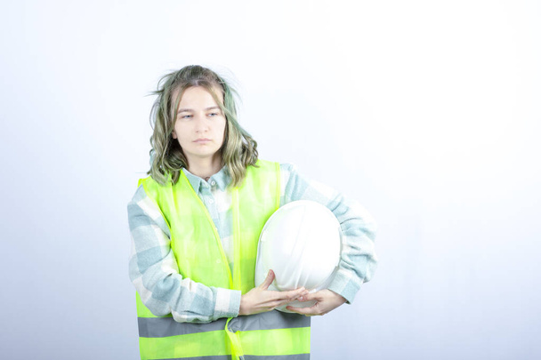 Foto eines jungen Bauarbeiters in grüner Weste, der einen Hut auf weißem Hintergrund hält. Hochwertiges Foto - Foto, Bild