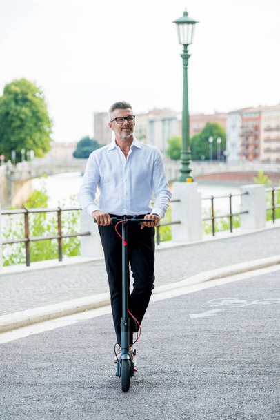 Young businessman in a suit riding an electric scooter while commuting to work in city. Ecological transportation concept - Foto, Imagem
