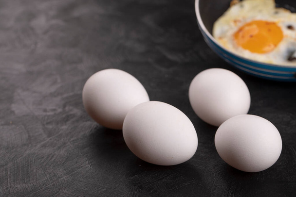 Πεντανόστιμα τηγανητά αυγά σε τηγάνι με ωμά λευκά αυγά στη μαύρη επιφάνεια. Υψηλής ποιότητας φωτογραφία - Φωτογραφία, εικόνα