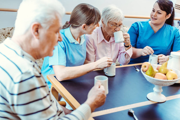 Seniors and caregivers having coffee time in the nursing home - Foto, imagen