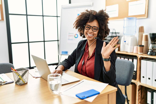 African american woman with afro hair working at the office wearing operator headset waiving saying hello happy and smiling, friendly welcome gesture  - Foto, afbeelding