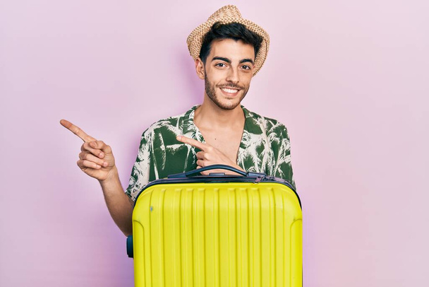 Молодой латиноамериканец, одетый в летний стиль и держащий сумку, улыбающийся и смотрящий на камеру, указывая двумя руками и пальцами в сторону.  - Фото, изображение