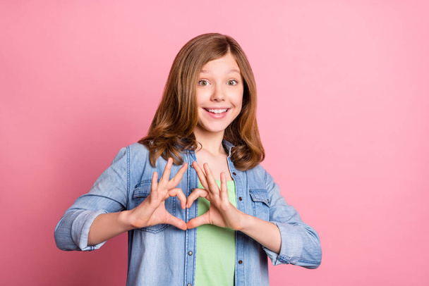 Photo portrait girl smiling showing heart sign with fingers dreamy happy isolated pastel pink color background - Fotografie, Obrázek