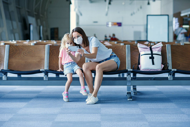 Mother with daughter in masks waiting for their flight at airport. Woman with little girl in international airport. - Foto, Imagem