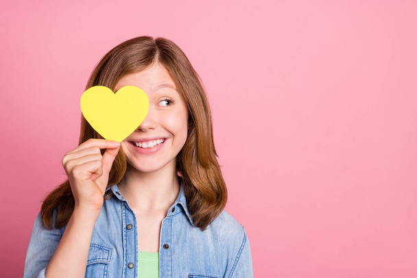 Photo portrait girl smiling hiding eye behind yellow heart postcard looking copyspace isolated pastel pink color background - Fotoğraf, Görsel