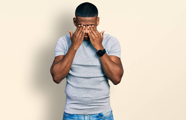 Jonge zwarte man draagt casual t-shirt wrijven ogen voor vermoeidheid en hoofdpijn, slaperige en vermoeide uitdrukking. gezichtsproblemen  - Foto, afbeelding