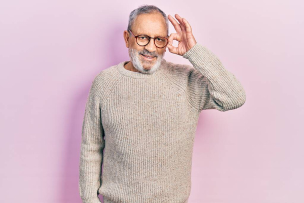 Handsome senior man with beard wearing casual sweater and glasses smiling positive doing ok sign with hand and fingers. successful expression.  - Foto, Imagem