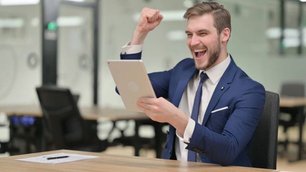 Успішний бізнесмен святкує перемогу на планшеті на роботі
  - Фото, зображення