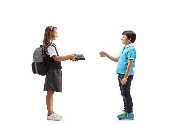 Schoolgirl giving books to a young boy isolated on white background - Photo, Image