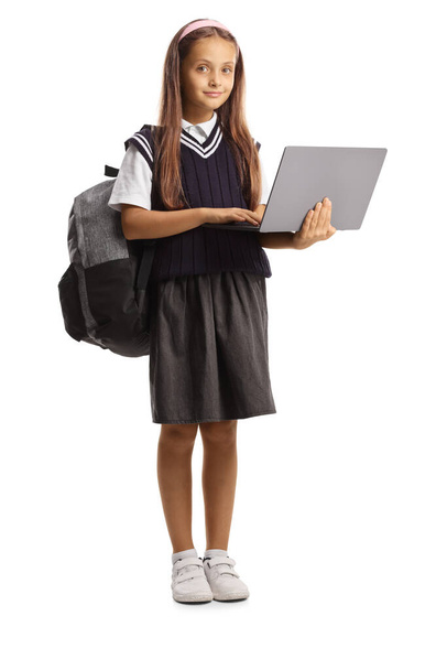 Schoolgirl in a school uniform holding a laptop computer and looking at camera isolated on white background - Photo, image